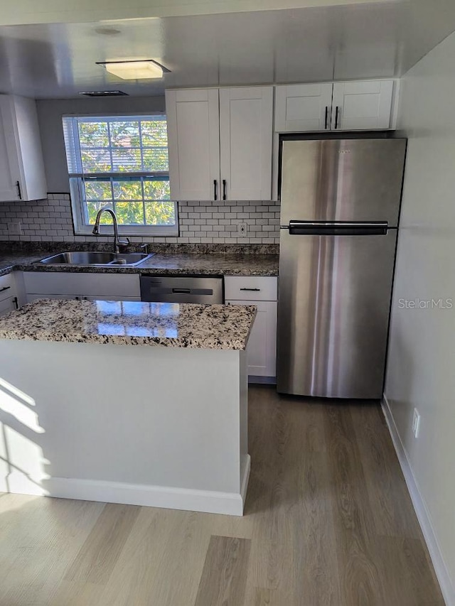 kitchen with appliances with stainless steel finishes, white cabinets, a sink, dark stone countertops, and wood finished floors