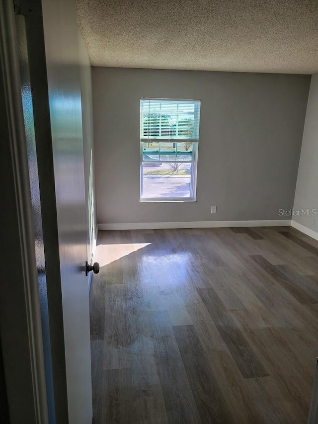 empty room featuring dark wood finished floors, a textured ceiling, and baseboards