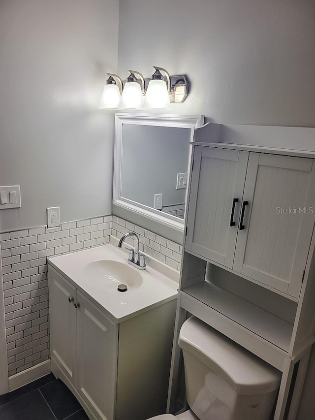 bathroom featuring wainscoting, toilet, tile patterned floors, vanity, and tile walls