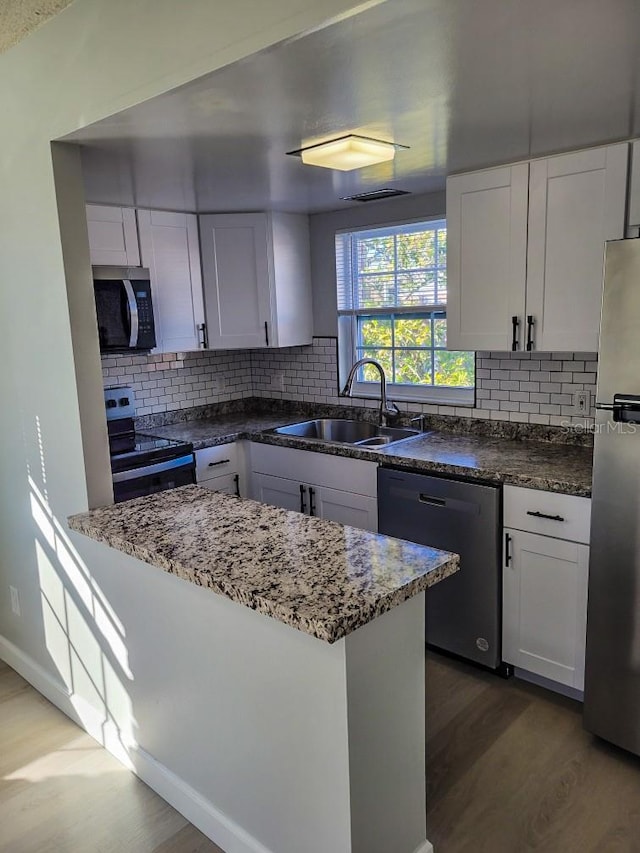 kitchen featuring wood finished floors, a sink, white cabinetry, appliances with stainless steel finishes, and backsplash