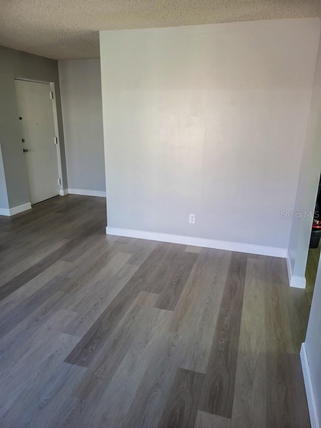 spare room with dark wood-style flooring, a textured ceiling, and baseboards