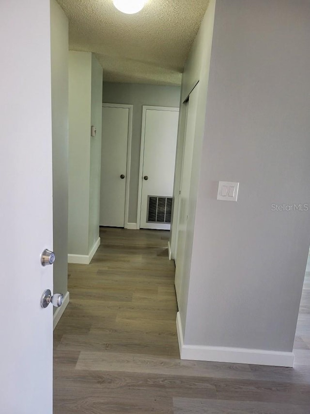 hallway with a textured ceiling, light wood finished floors, visible vents, and baseboards