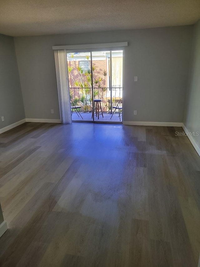 spare room with a textured ceiling, baseboards, and dark wood-style flooring