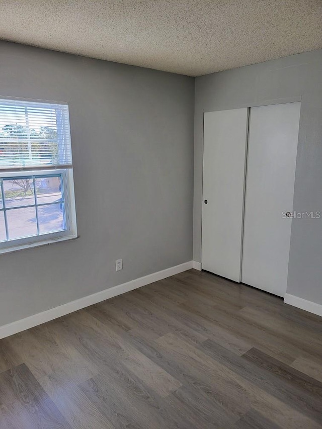 unfurnished bedroom featuring a closet, a textured ceiling, baseboards, and wood finished floors