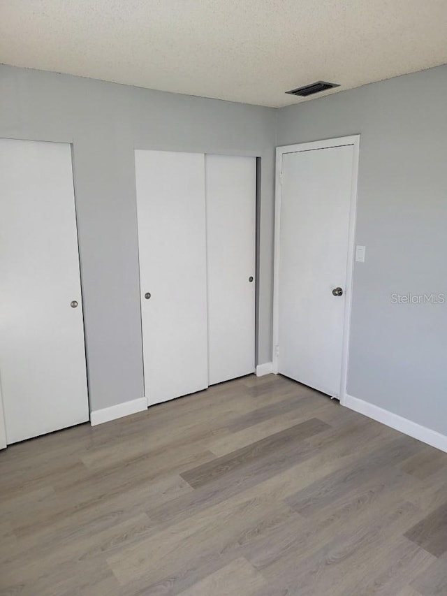 unfurnished bedroom featuring a textured ceiling, visible vents, baseboards, light wood-type flooring, and two closets