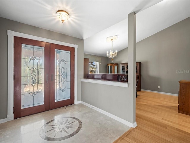 foyer entrance featuring baseboards, lofted ceiling, wood finished floors, french doors, and a notable chandelier