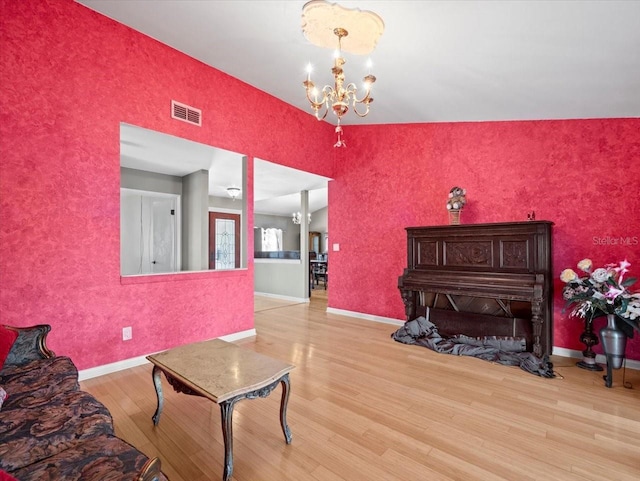 living area featuring baseboards, wood finished floors, visible vents, and a notable chandelier