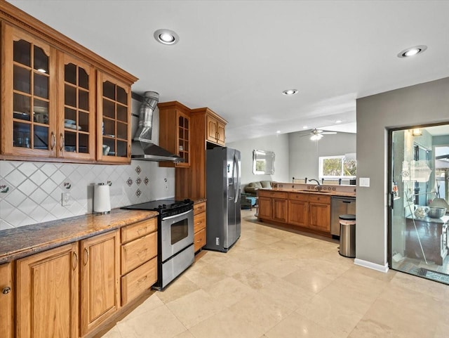 kitchen featuring backsplash, appliances with stainless steel finishes, glass insert cabinets, a sink, and wall chimney exhaust hood