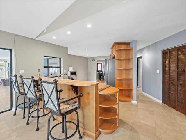 kitchen featuring freestanding refrigerator, plenty of natural light, a kitchen bar, and open shelves