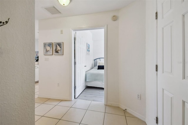 hall with light tile patterned floors, visible vents, and baseboards