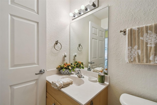 half bathroom featuring a textured wall, vanity, and toilet