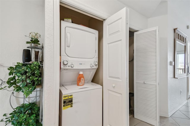 clothes washing area with light tile patterned floors, laundry area, stacked washing maching and dryer, and baseboards