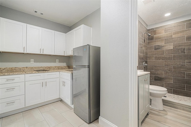 kitchen with freestanding refrigerator, white cabinetry, and visible vents