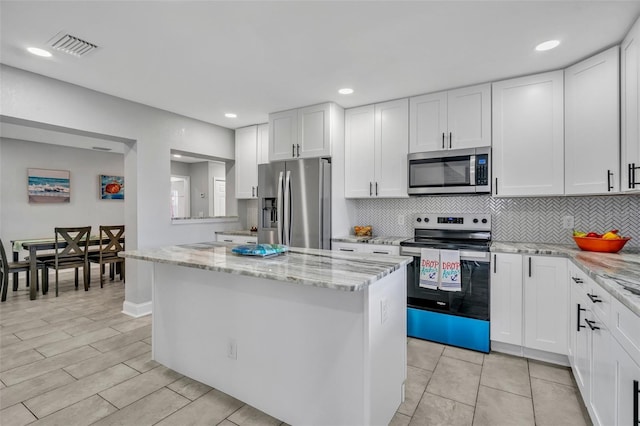 kitchen with stainless steel appliances, white cabinetry, a kitchen island, and light stone countertops