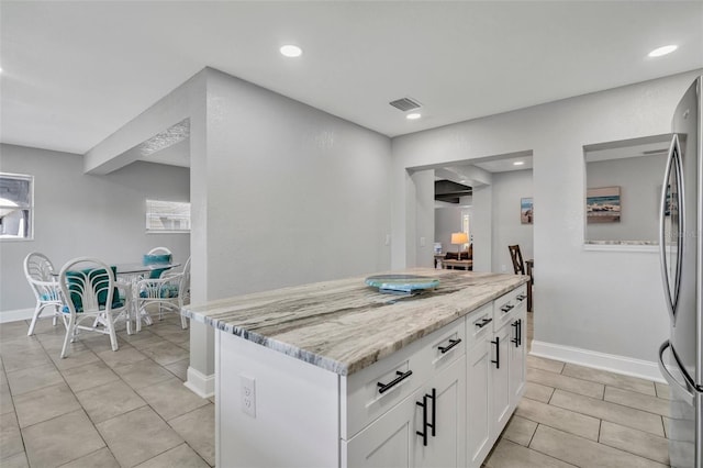 kitchen featuring light stone counters, visible vents, freestanding refrigerator, white cabinets, and baseboards