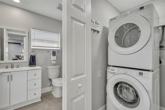 laundry area featuring light tile patterned floors, stacked washer / drying machine, a sink, laundry area, and baseboards