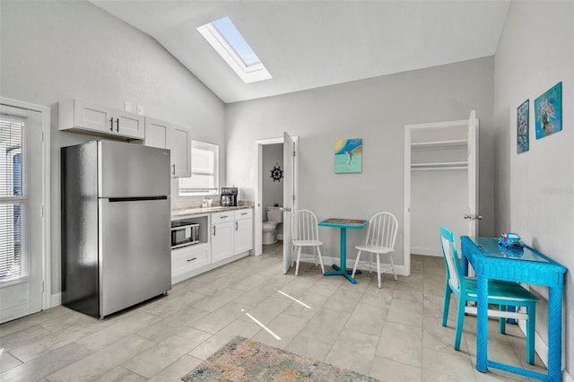 kitchen with stainless steel appliances, vaulted ceiling with skylight, white cabinetry, and baseboards