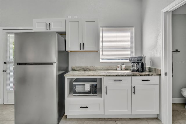 kitchen featuring light tile patterned floors, white cabinetry, appliances with stainless steel finishes, and light stone counters