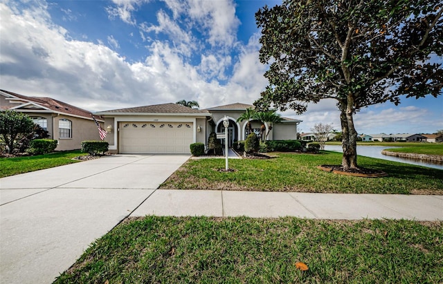 view of front facade with stucco siding, a water view, an attached garage, a front yard, and driveway