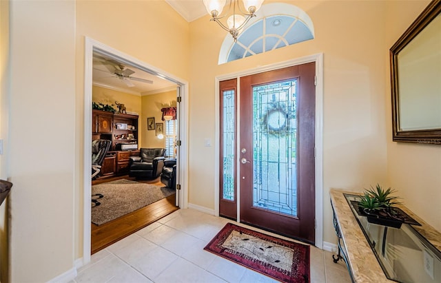 entryway featuring baseboards, ceiling fan with notable chandelier, ornamental molding, and light tile patterned flooring