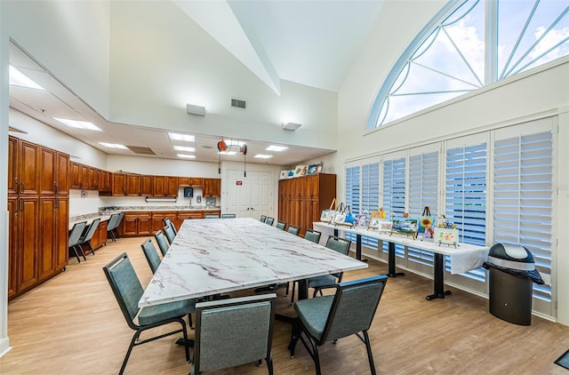 dining room with high vaulted ceiling, light wood-style flooring, visible vents, and a workshop area