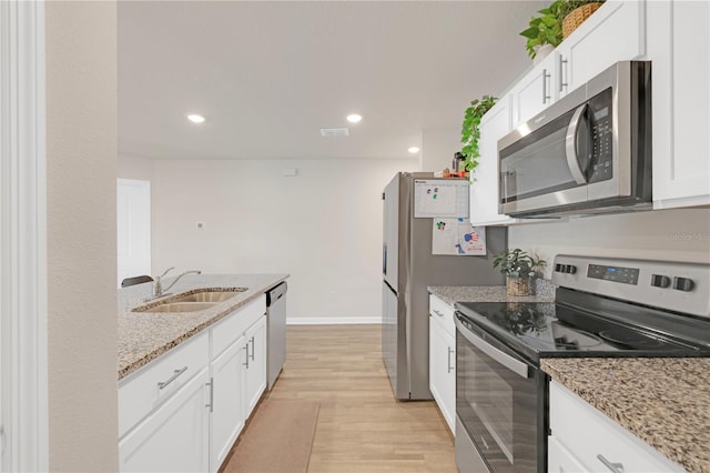 kitchen featuring light stone counters, light wood-style flooring, appliances with stainless steel finishes, white cabinetry, and a sink