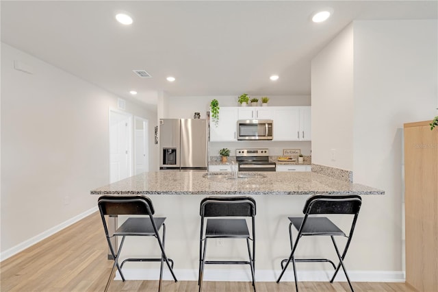 kitchen featuring visible vents, appliances with stainless steel finishes, a kitchen breakfast bar, a peninsula, and light stone countertops