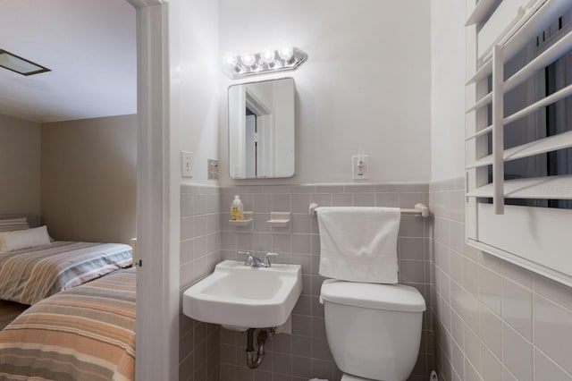 bathroom featuring a wainscoted wall, a sink, tile walls, and toilet