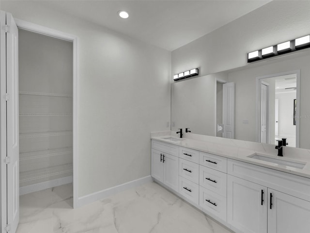 full bath with marble finish floor, a sink, baseboards, and double vanity