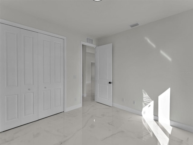 unfurnished bedroom with a closet, marble finish floor, visible vents, and baseboards