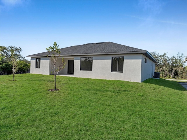 rear view of property featuring central air condition unit, stucco siding, a lawn, and roof with shingles