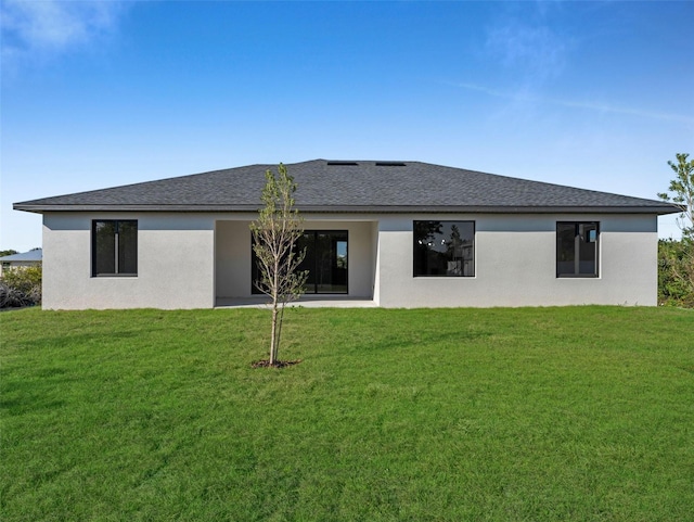 back of house with a yard, a shingled roof, and stucco siding