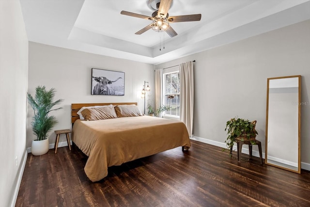 bedroom featuring dark wood-style floors, baseboards, a raised ceiling, and a ceiling fan