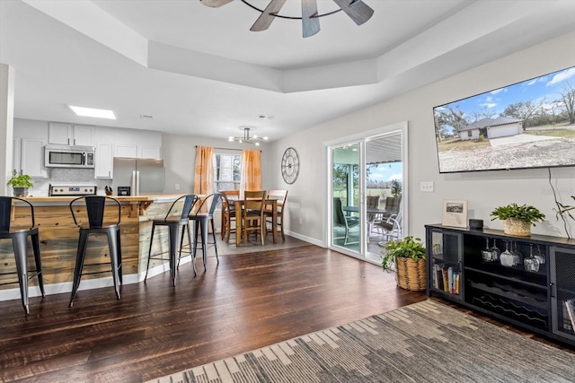 kitchen with dark wood-style floors, stainless steel appliances, a raised ceiling, white cabinets, and a kitchen bar