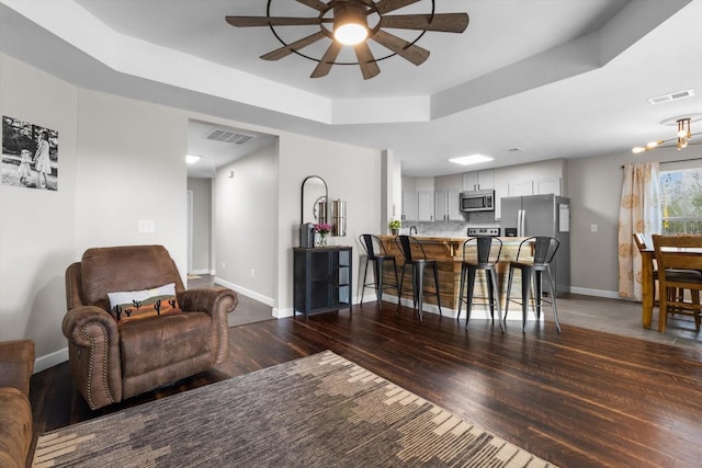 living room featuring dark wood-style floors, a tray ceiling, visible vents, and baseboards