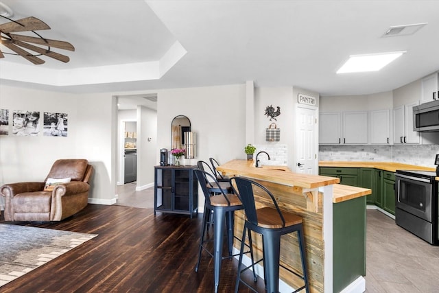 kitchen featuring stainless steel appliances, decorative backsplash, green cabinets, open floor plan, and wood counters