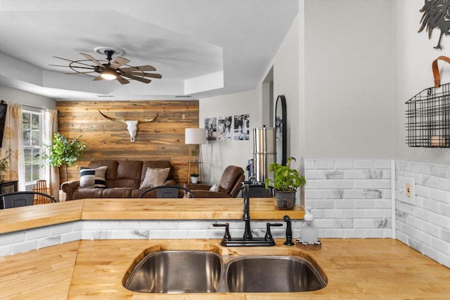 kitchen featuring open floor plan, a sink, wood walls, ceiling fan, and wood finished floors