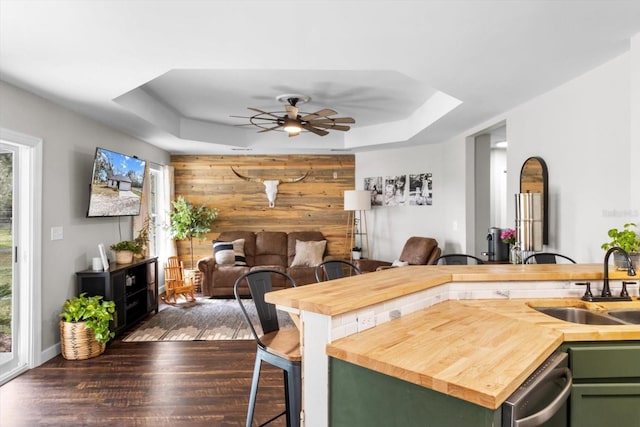 kitchen with a raised ceiling, green cabinetry, dark wood-style floors, a kitchen bar, and a sink