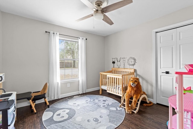 bedroom featuring dark wood-type flooring, ceiling fan, a crib, and baseboards