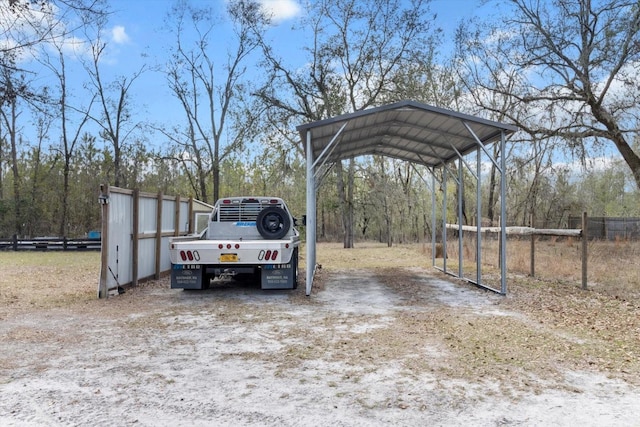 view of car parking featuring dirt driveway, fence, and a detached carport