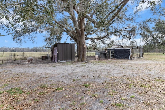 view of yard with an outbuilding, a rural view, exterior structure, fence, and a detached carport