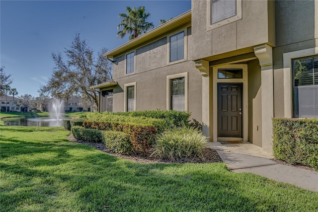 property entrance with a water view, a yard, and stucco siding