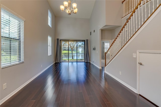 foyer entrance featuring baseboards, dark wood-style floors, an inviting chandelier, stairs, and a high ceiling