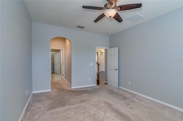 unfurnished bedroom featuring baseboards, visible vents, arched walkways, light colored carpet, and ceiling fan