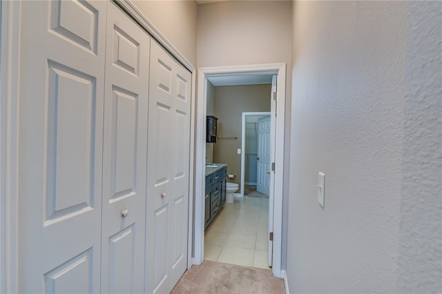 hallway featuring light carpet, a textured wall, and baseboards