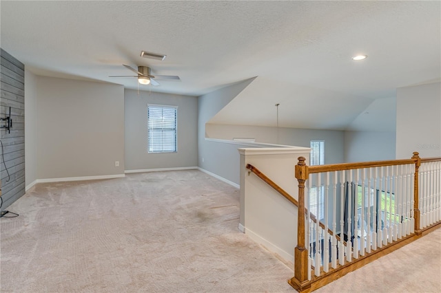 hall with a textured ceiling, an upstairs landing, visible vents, baseboards, and carpet