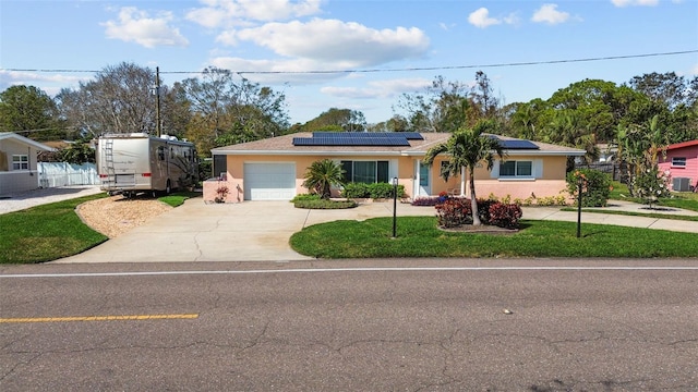 single story home with an attached garage, concrete driveway, roof mounted solar panels, stucco siding, and a front lawn