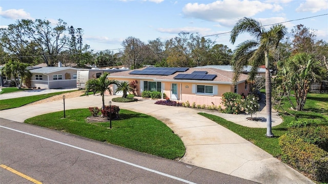 ranch-style house with driveway, brick siding, roof mounted solar panels, and a front yard