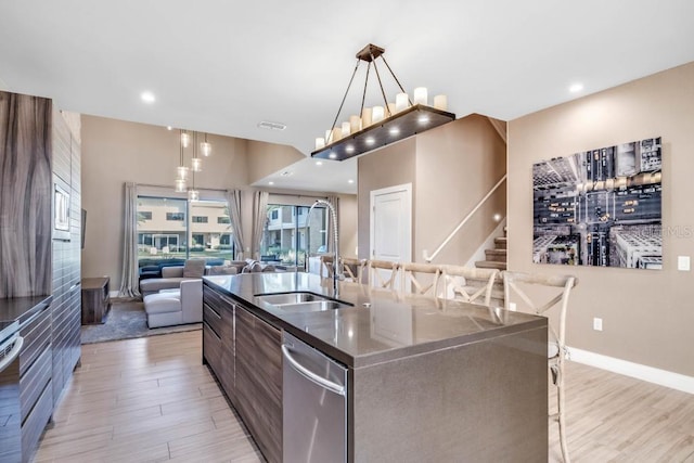 kitchen featuring a center island with sink, light wood-style floors, open floor plan, a sink, and dishwasher