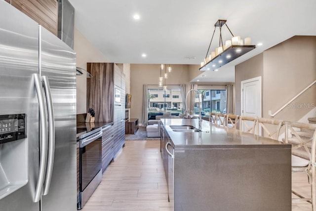 kitchen featuring pendant lighting, stainless steel appliances, dark countertops, a sink, and a large island with sink